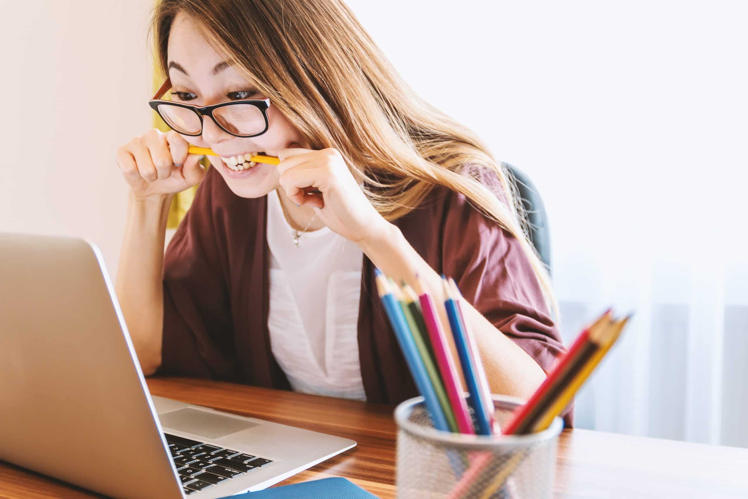Young woman focused on laptop at a creative workspace, with colorful pencils and natural light.