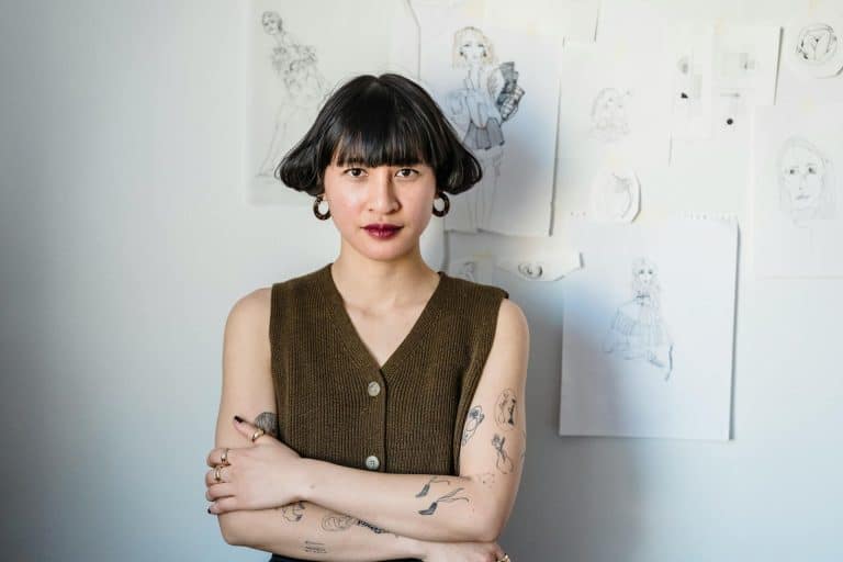 Confident young artist with bob hairstyle in creative space surrounded by her sketches.