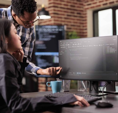 Diverse programmers discussing about html code compiling discovers errors, standing in front of multiple screens in startup office. Software developers working on server interface development.